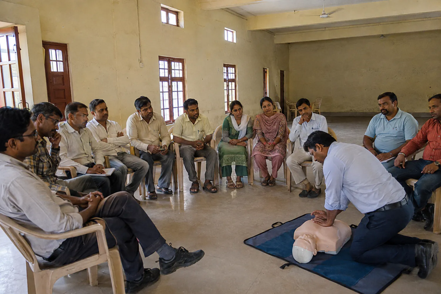 Illustration: a first-aid session, an instructor demonstrating CPR to seated participants